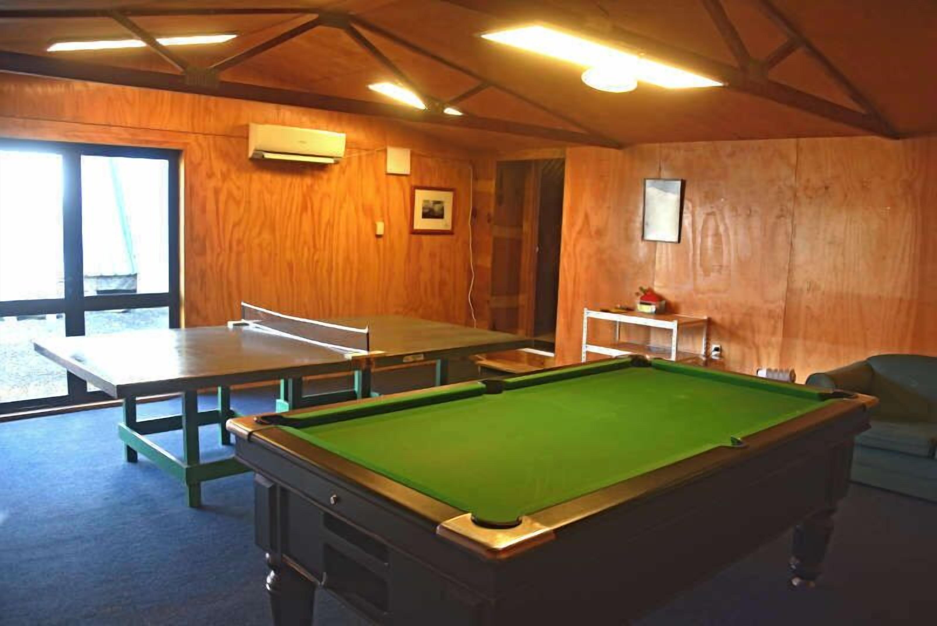 Una mesa de billar en una habitación con paredes de madera y un ventanal grande.