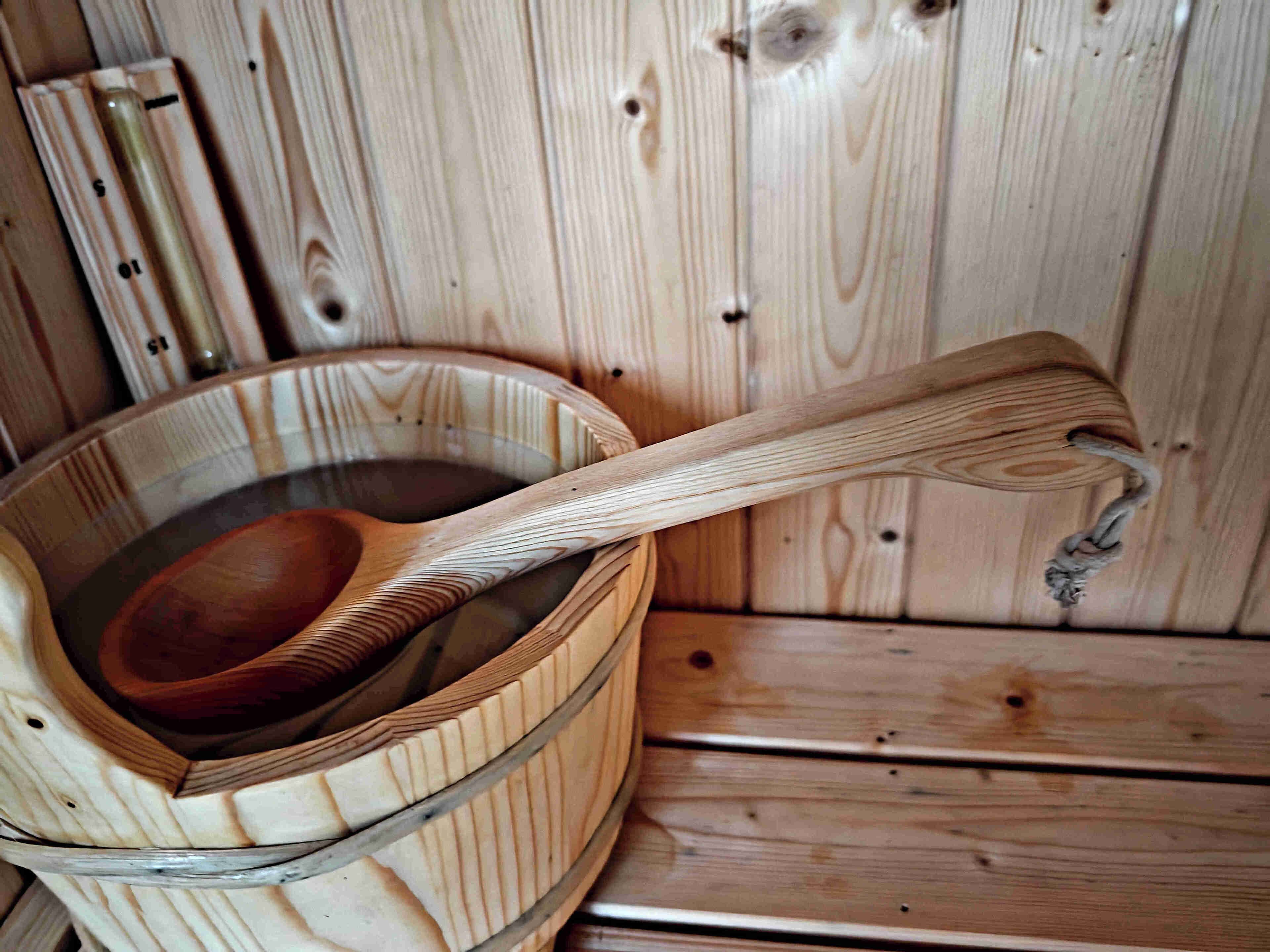 A wooden tub with a wooden ladle inside, set against a wooden wall.