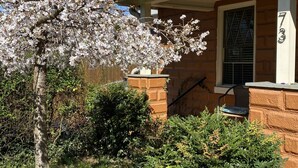 Une maison d’habitation avec une façade en briques, un porche et un arbre aux fleurs blanches devant.