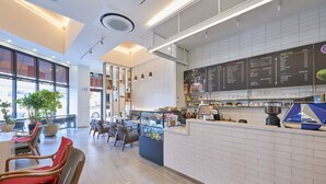 L’intérieur d’un café moderne, avec un comptoir, un tableau affichant le menu, un espace salon et des plantes en pot.
