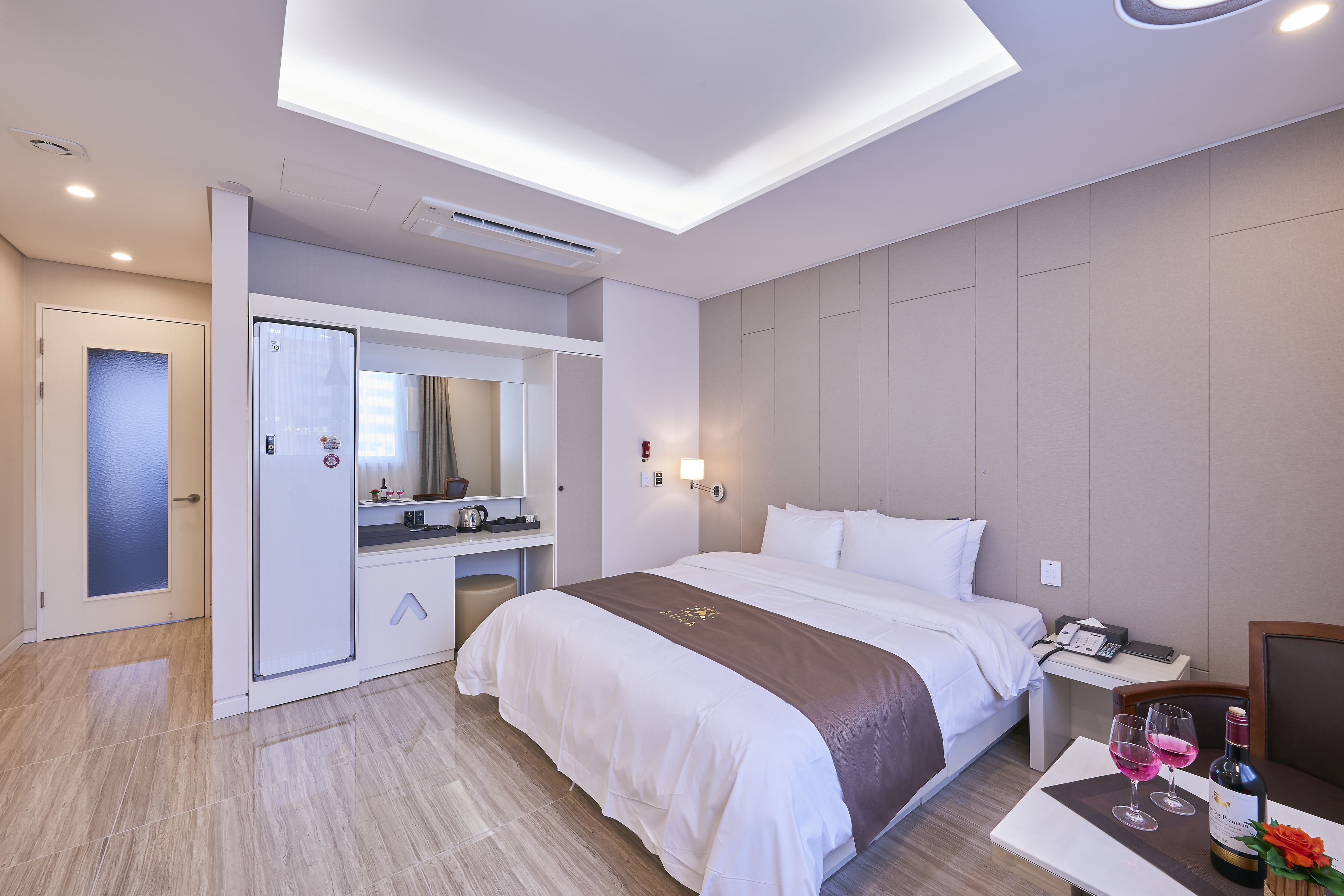 A hotel room with a bed, a desk, a mirror, and a table with wine glasses.