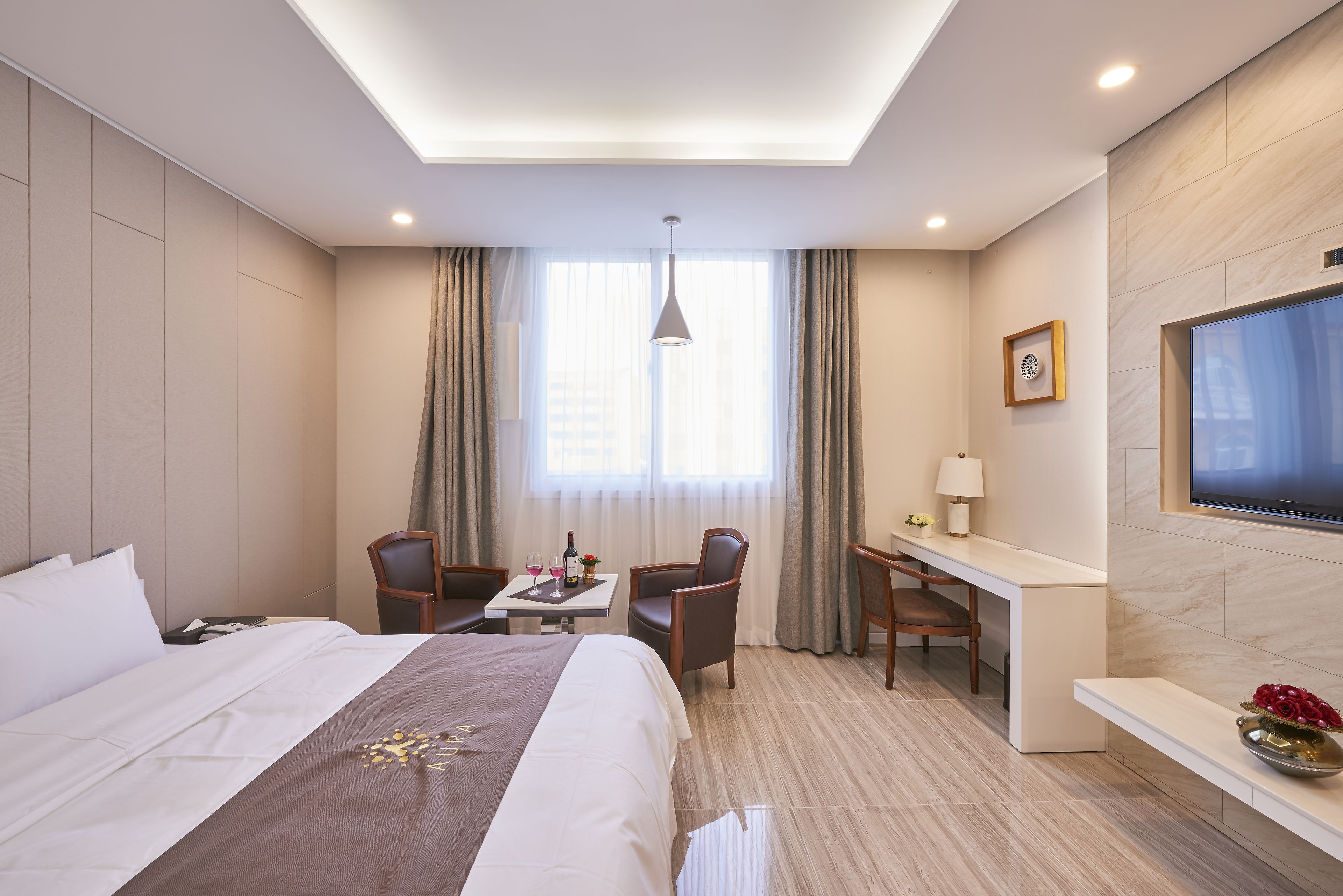 A hotel room with a bed, a desk, two chairs, a TV, and a window with curtains.