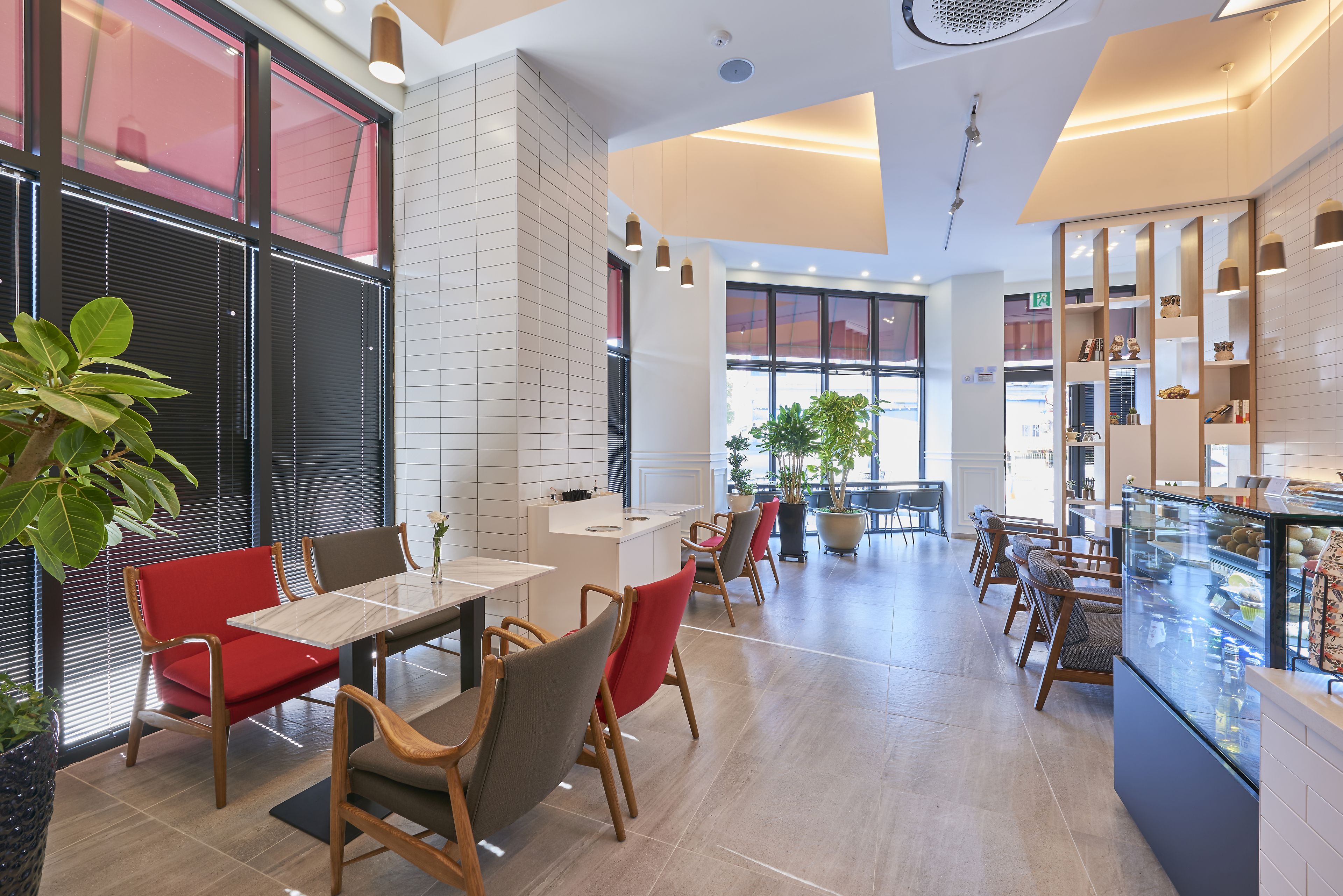 A modern cafe with a long counter, red and grey chairs, and a display case with pastries.