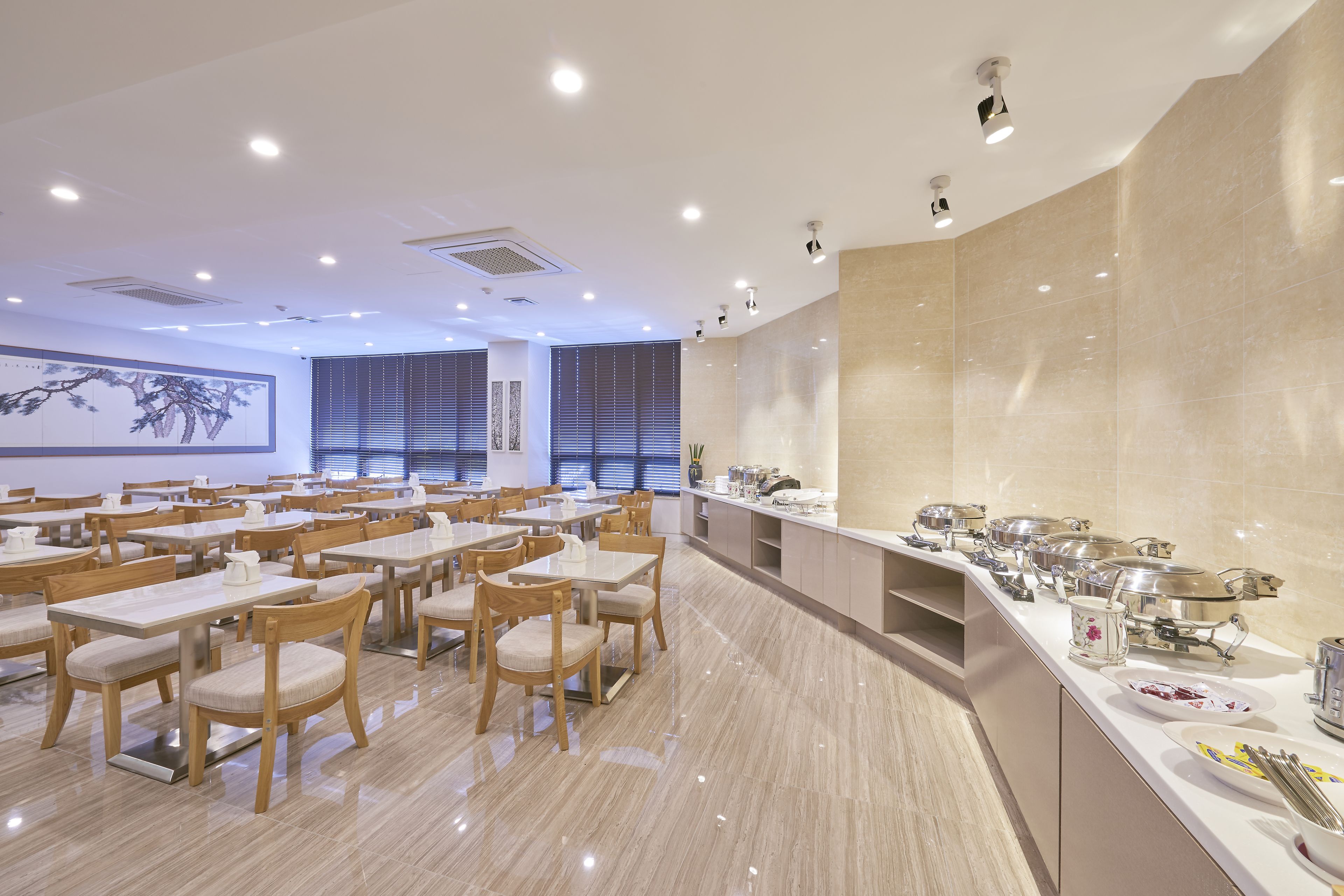 A spacious dining area with multiple tables and chairs, a buffet line with various food items, and a large wall with a framed artwork.