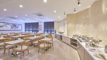 A spacious dining area with multiple tables and chairs, a buffet line with various food items, and a large wall with a framed artwork.