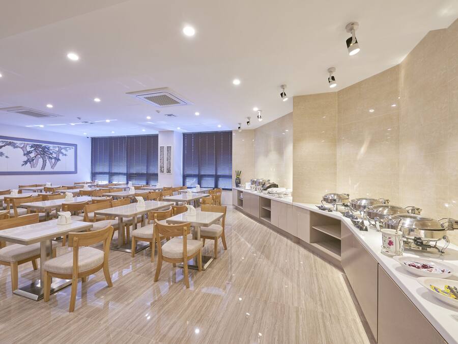 A spacious dining area with multiple tables and chairs, a buffet line with various food items, and a large wall with a framed artwork.