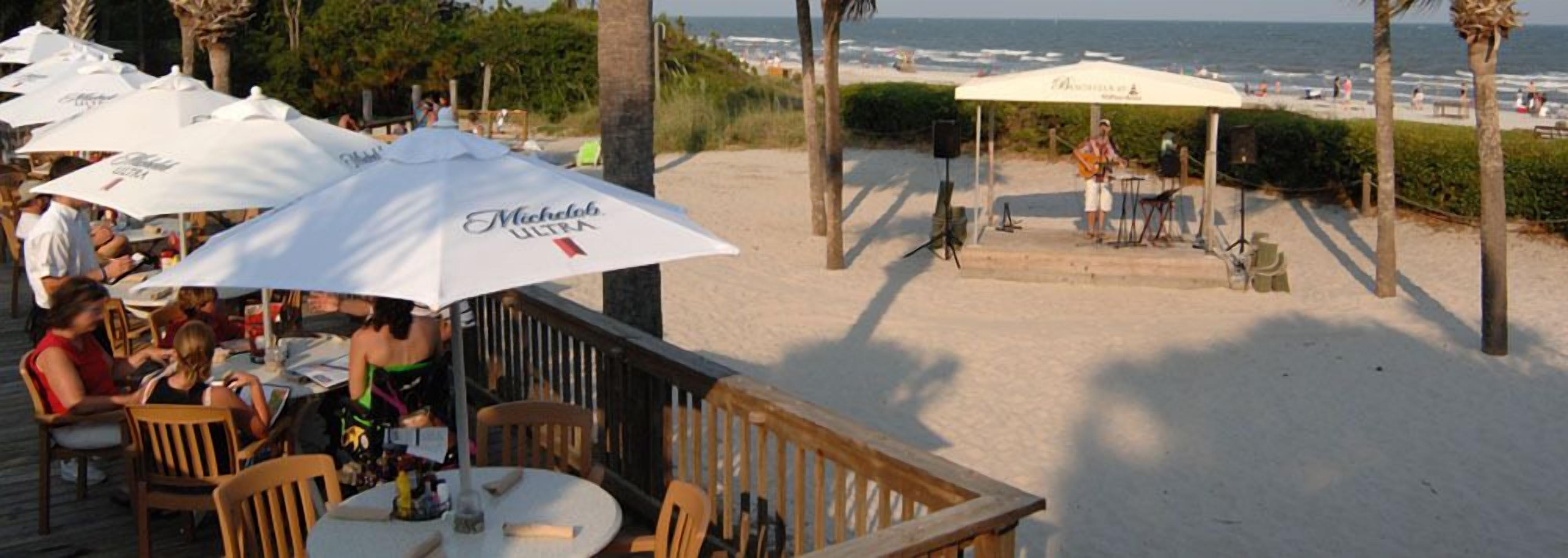 Espace extérieur avec parasols, vue sur la plage et scène pour des concerts.