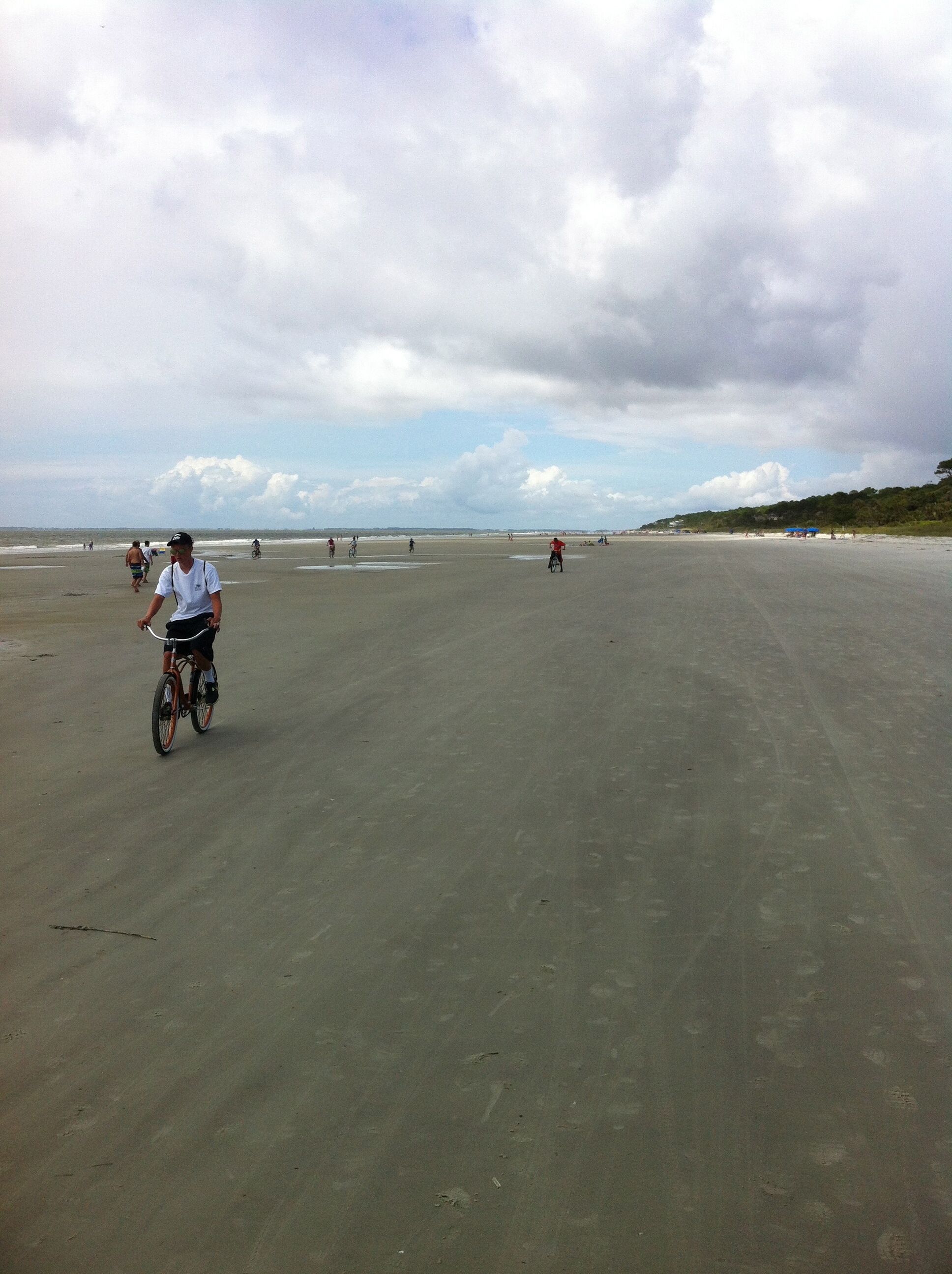 Una playa amplia y abierta con gente caminando y andando en bicicleta.
