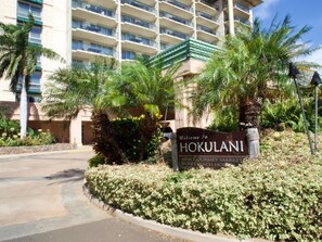 A sign welcoming to HOKULANI with a view of a multi-story building and palm trees.