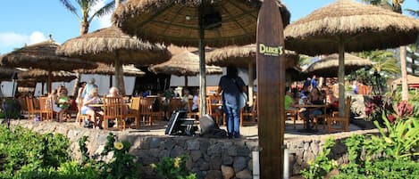 An outdoor dining area with thatched umbrellas and stone walls.