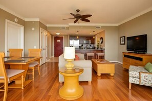 A spacious living room with a dining area, a kitchen in the background, and a television on the right.