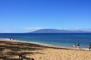 Una playa con gente caminando por la orilla, una montaña al fondo y cielos despejados.