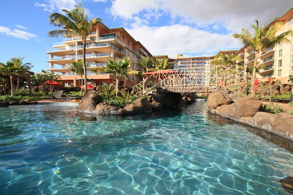 A hotel pool area with clear water, palm trees, and a bridge.