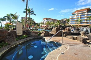 Un área de piscina con jacuzzi, palmeras y una cascada.
