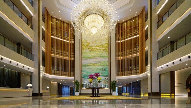 A spacious lobby with a large chandelier, a reception desk, and a mural on the wall. - Qingshan Hotel Baotou（Yingbin Building） (Baotou)