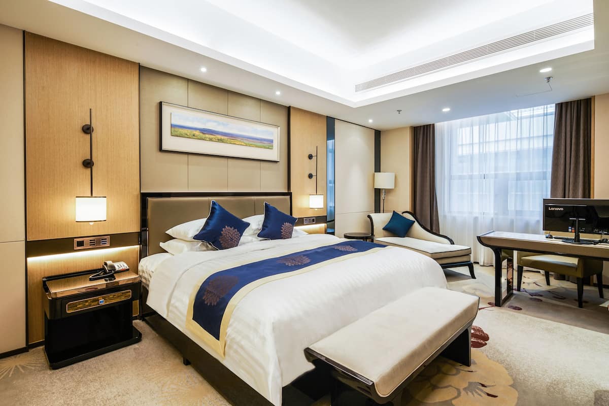 A hotel room with a large bed, bedside tables, a desk, and a television.