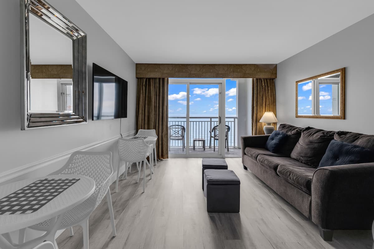A modern living room with a grey sofa, a white table, and a balcony with a view.