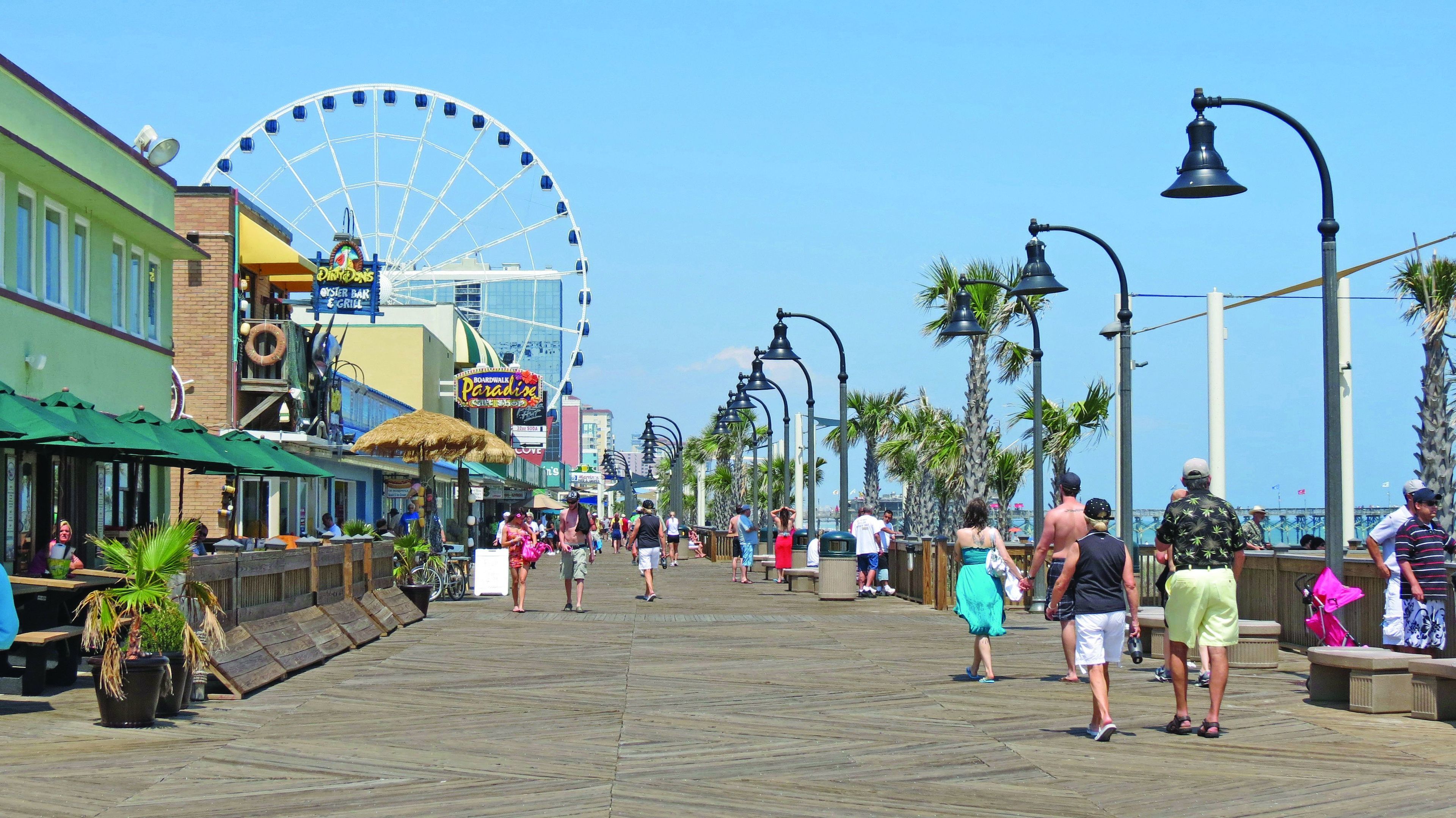 A boardwalk with shops, a Ferris wheel, and palm trees.