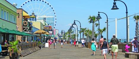 A boardwalk with shops, a Ferris wheel, and palm trees.