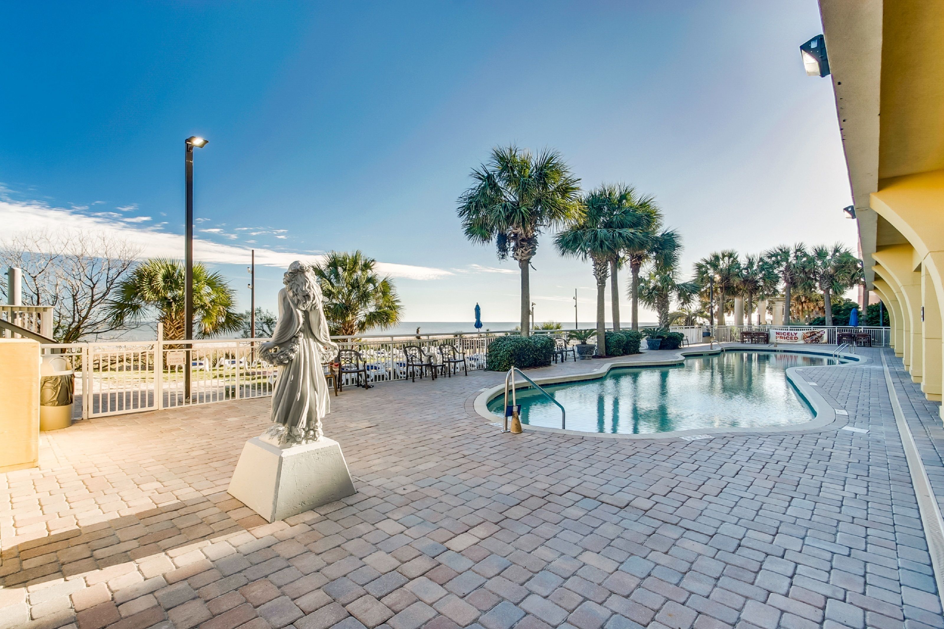 A poolside area with a statue, palm trees, and a view of the ocean.