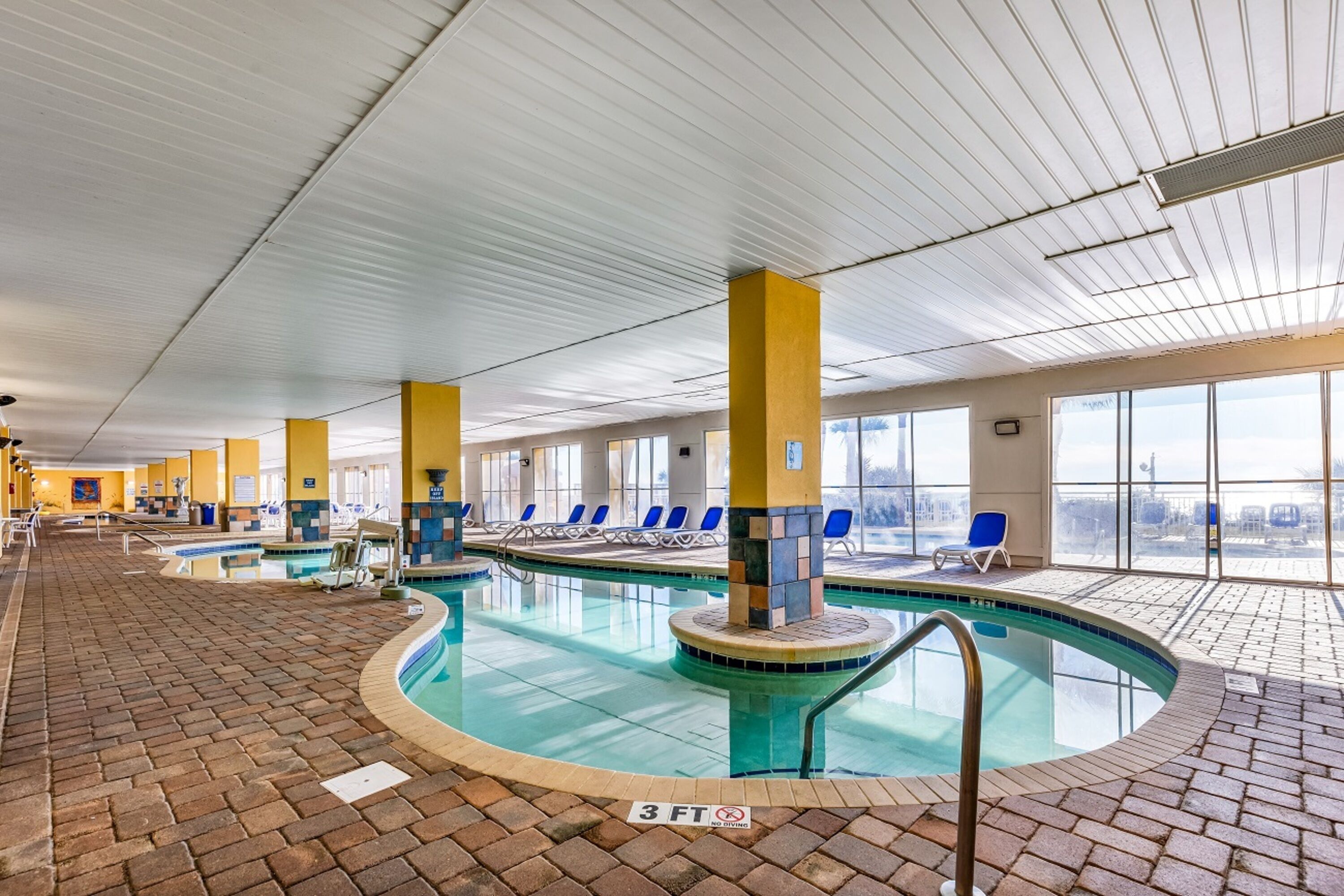 An indoor swimming pool with clear water, yellow pillars, and blue lounge chairs.