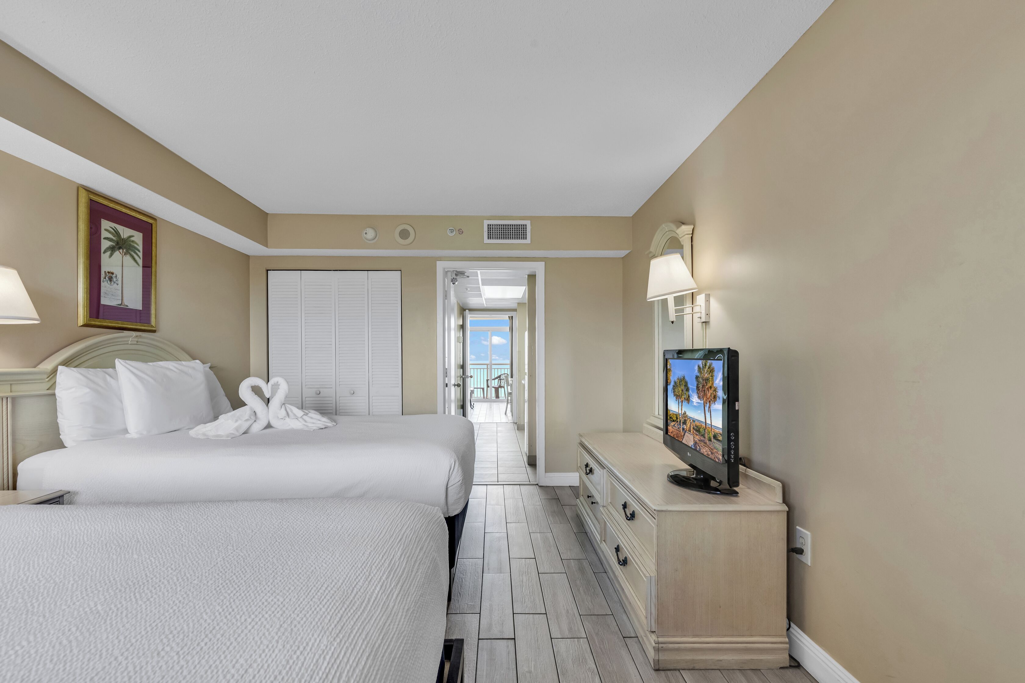 Quarto de hotel com duas camas, televisão, cómoda e vista para a varanda.