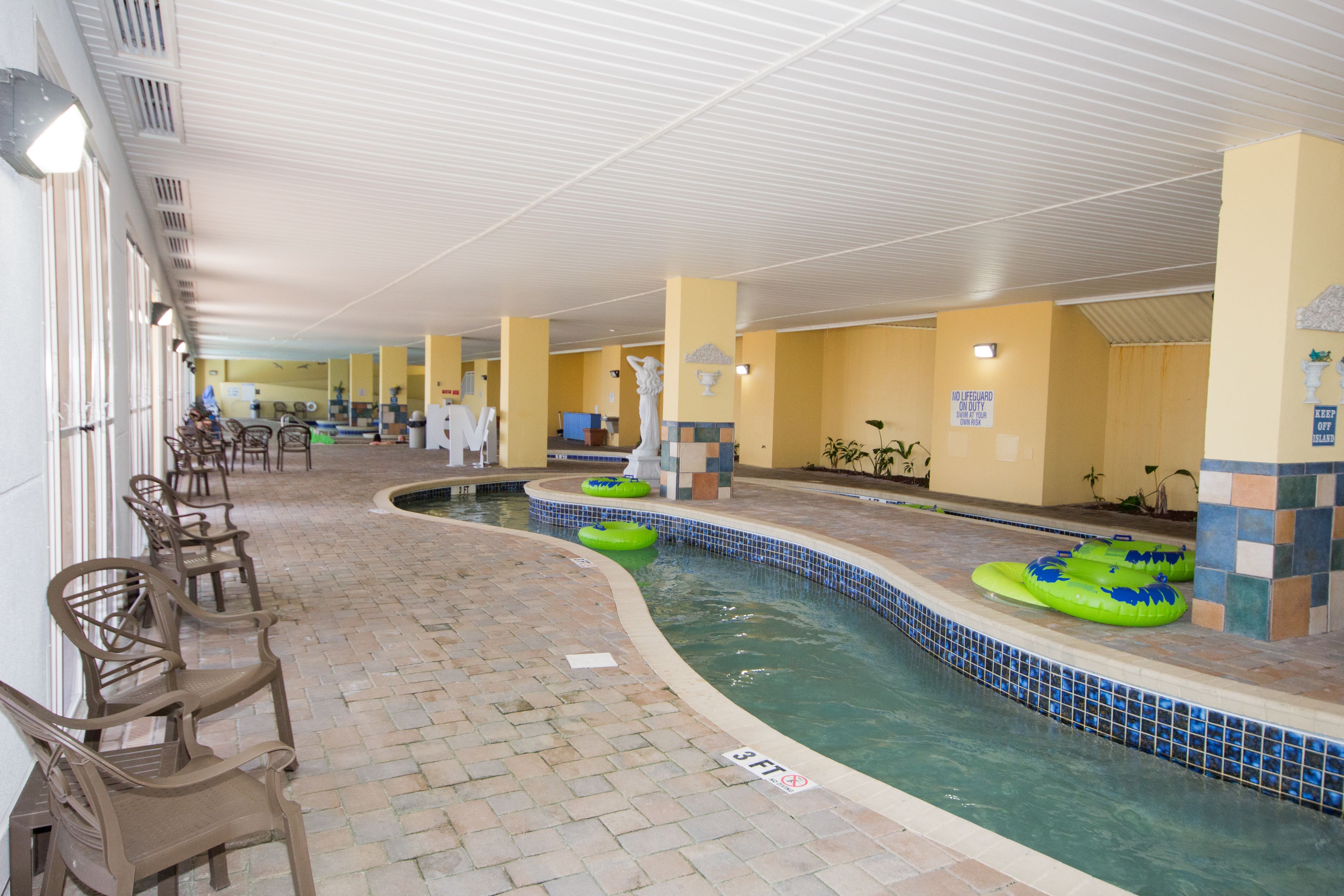An indoor swimming pool with green inflatable rings, chairs along the poolside, and a tiled floor.