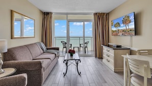 Varanda com vista para o mar, um sofá, uma mesa com um vaso de flores, uma televisão e um espaço de jantar.
