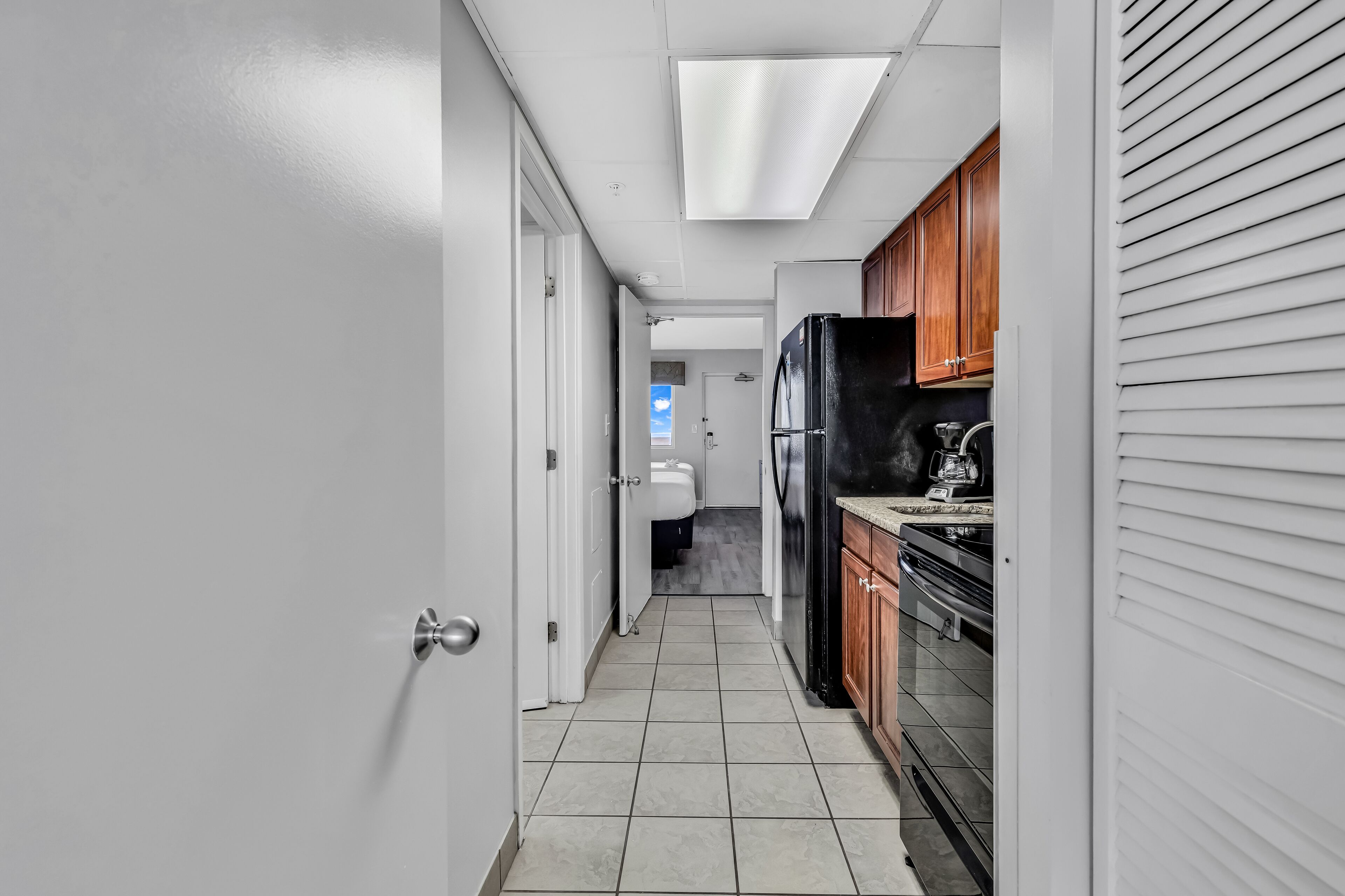 A narrow hallway with a kitchen area on the right, featuring a refrigerator, stove, and cabinets.