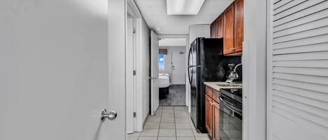 A narrow hallway with a kitchen area on the right, featuring a refrigerator, stove, and cabinets.
