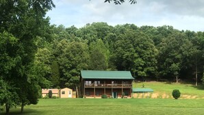 Une cabane en rondins à deux étages, dotée d’un toit végétalisé, entourée d’une pelouse bien entretenue et d’une forêt dense.