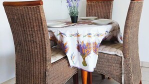 A dining area with a round table covered by a floral tablecloth, surrounded by four wicker chairs with wooden legs. - Antibes, Secure 1 bedroom apt, Sea Views, Swimming Pool, 3 adults - own parking (Antibes)