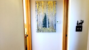 Un pasillo con suelo de madera, un cuadro de un bosque y una decoración de ciervo montada en la pared.