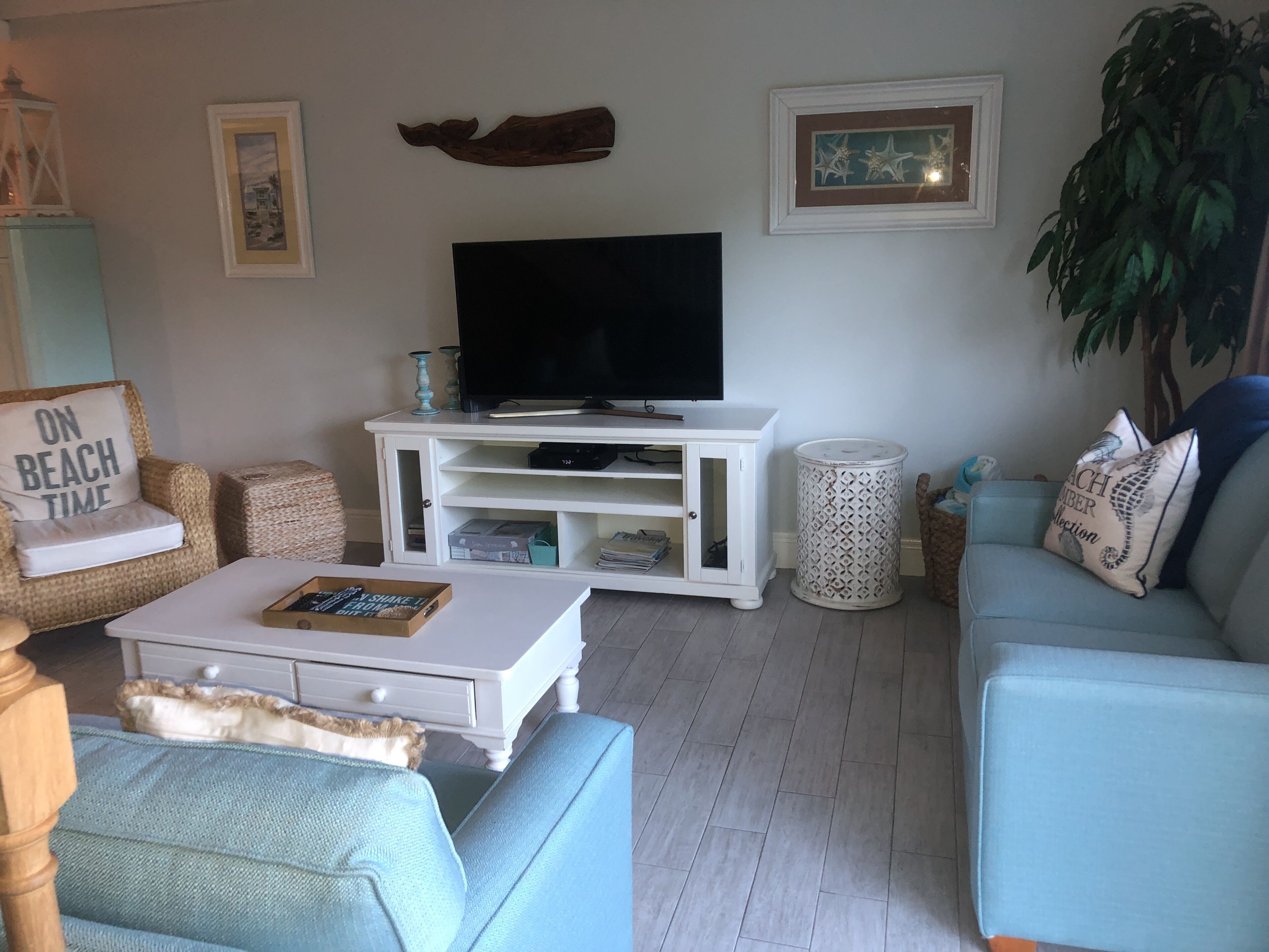 A living room with a white entertainment unit, a flat-screen TV, a blue sofa, and a wicker chair.