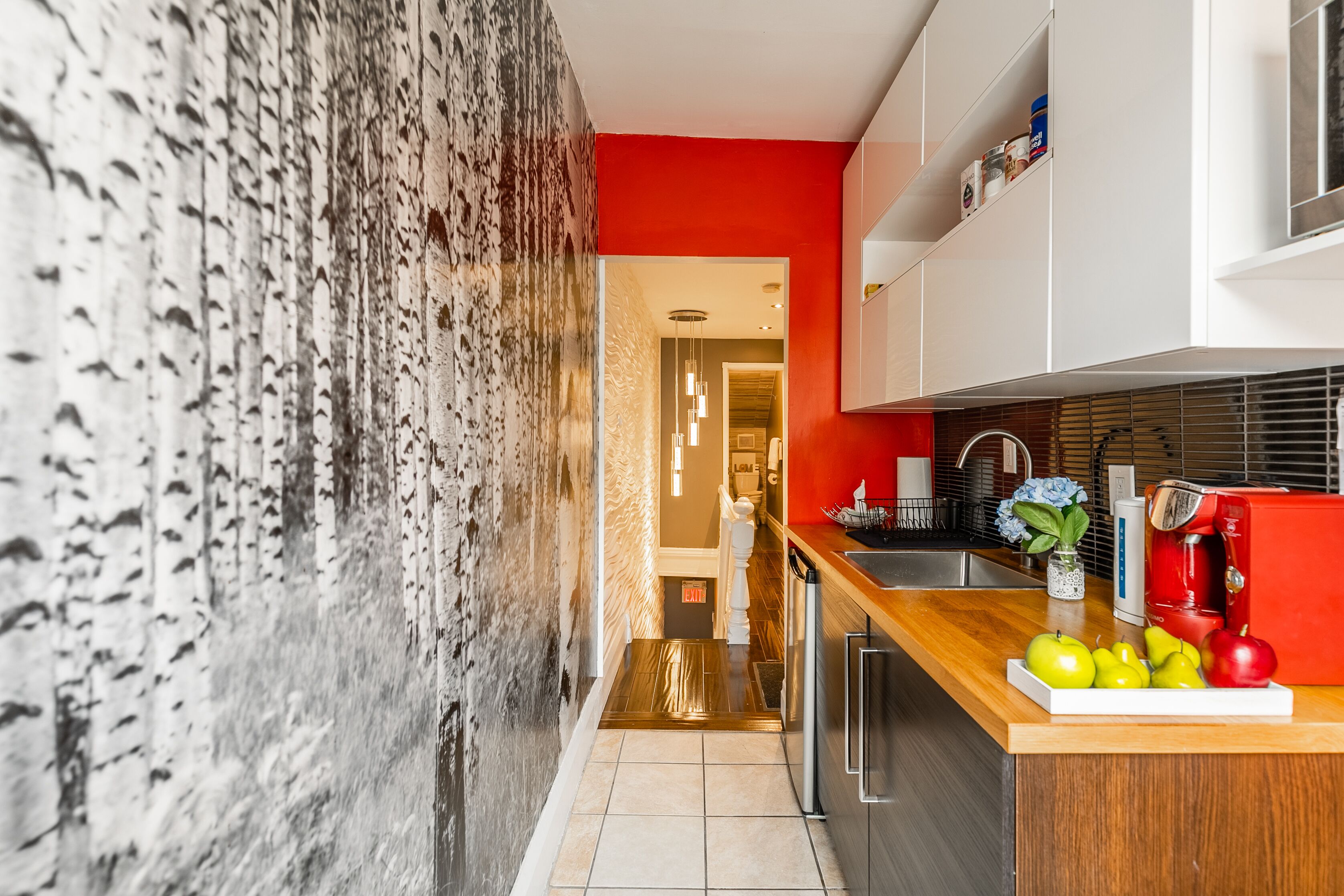 Una cocina moderna con una pared de acento roja, una encimera de madera y una variedad de frutas y verduras.