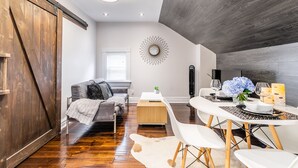 A modern living room with a wooden floor, a gray sofa, a white dining table with chairs, and a large mirror on the wall. - Boutique Penthouse Designer 1 BR Suite w/2 Balconies in Downtown Toronto (Toronto)