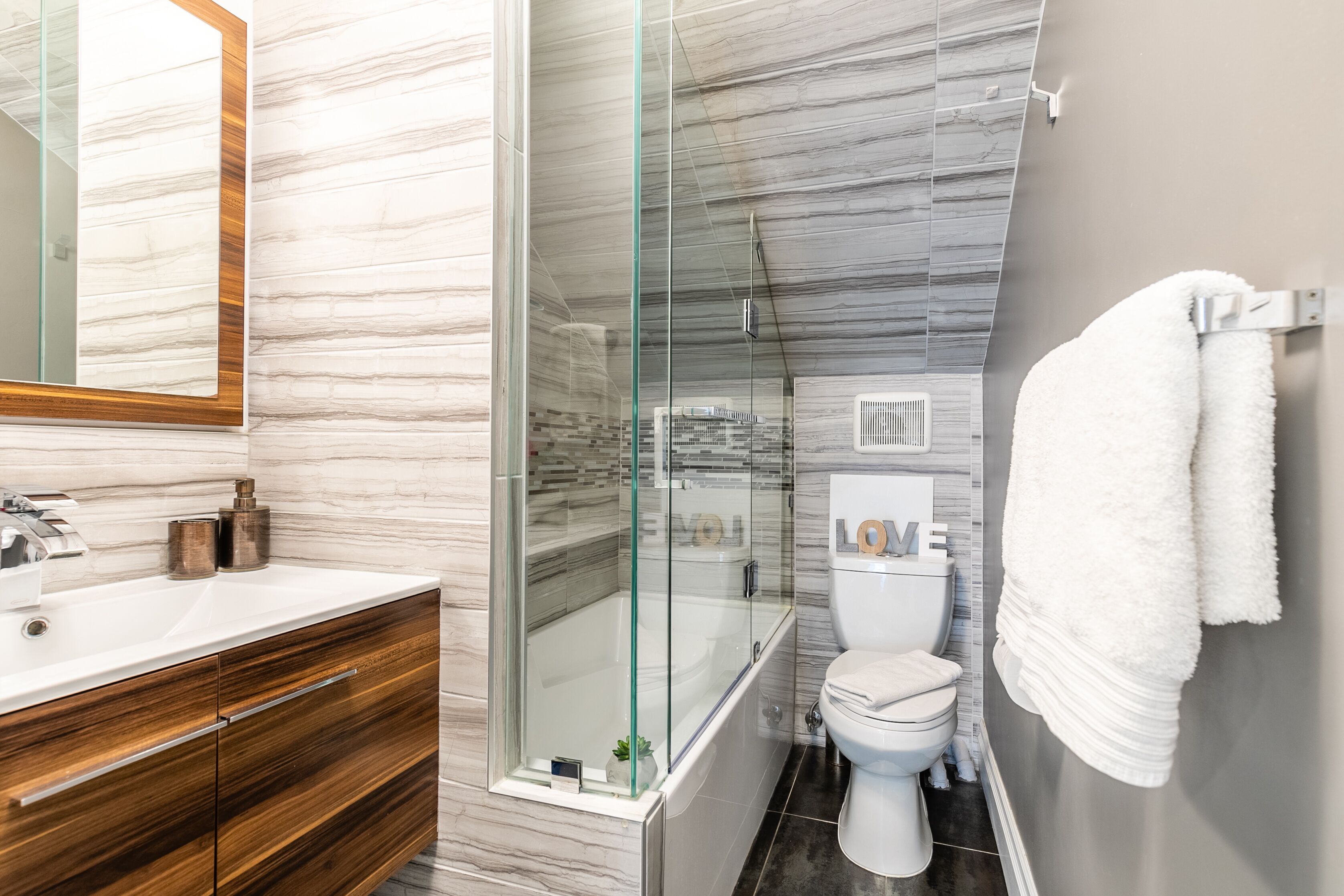 Ein modernes Badezimmer mit einer gläsernen Dusche, einem Holzbadezimmerhocker und einer weißen Toilette.