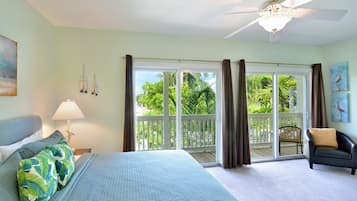 Une chambre à coucher comprenant un lit, une table de chevet, une lampe, un ventilateur de plafond et une vue sur un balcon avec une chaise.