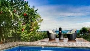 A pool area with two wicker chairs and a table, surrounded by lush greenery and a clear view of the mountains.