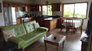 A kitchen with wooden cabinets, a green sofa, a dining table with chairs, and a TV.
