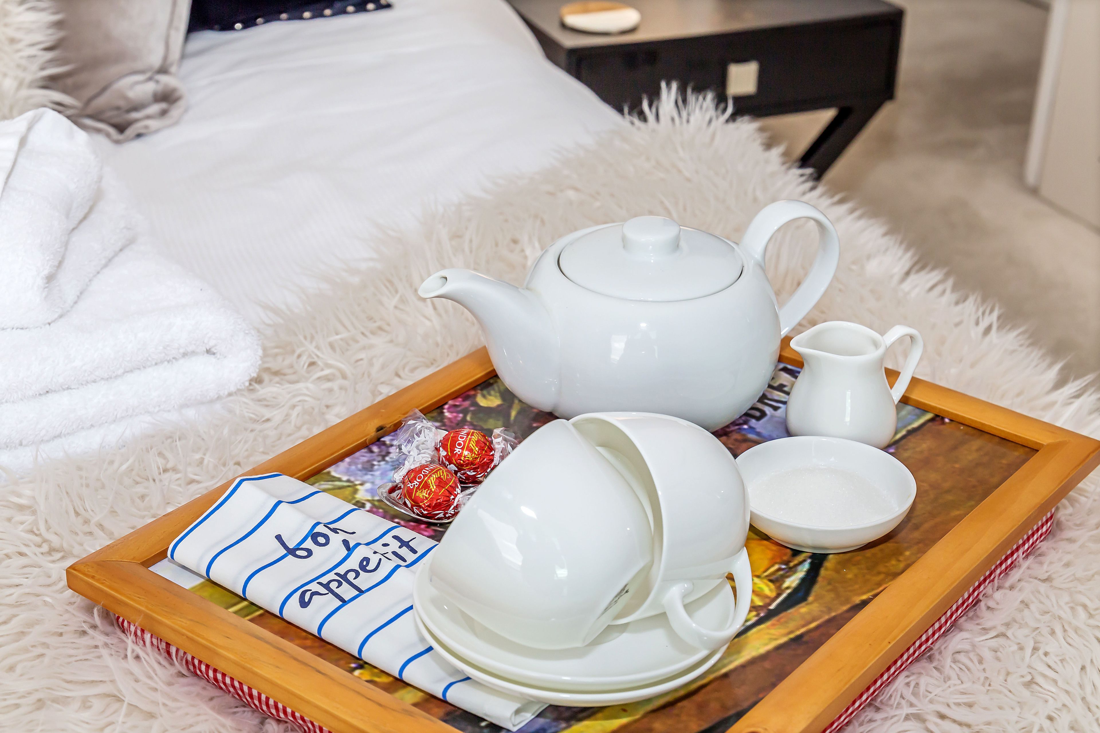 A tray with white teapot, cups, and a jug on a fluffy white surface.
