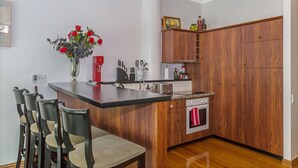 Une cuisine moderne avec des meubles en bois, un îlot central doté de tabourets de bar, un four encastré et un vase rempli de fleurs rouges.