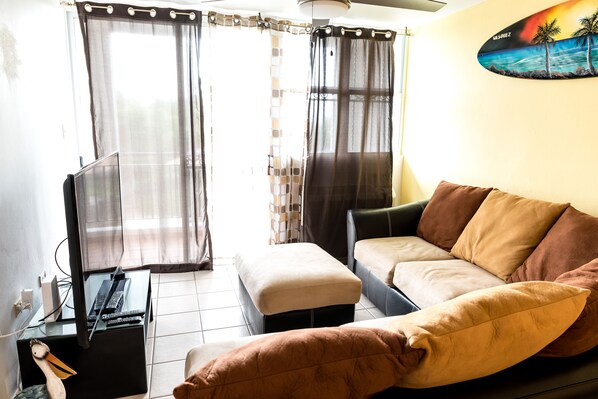 A living room with a sofa, ottoman, and a flat-screen TV on a stand.