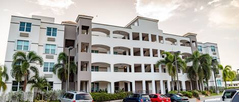 Un hotel de varios pisos con un diseño arquitectónico moderno, que cuenta con balcones y un estacionamiento con varios automóviles.