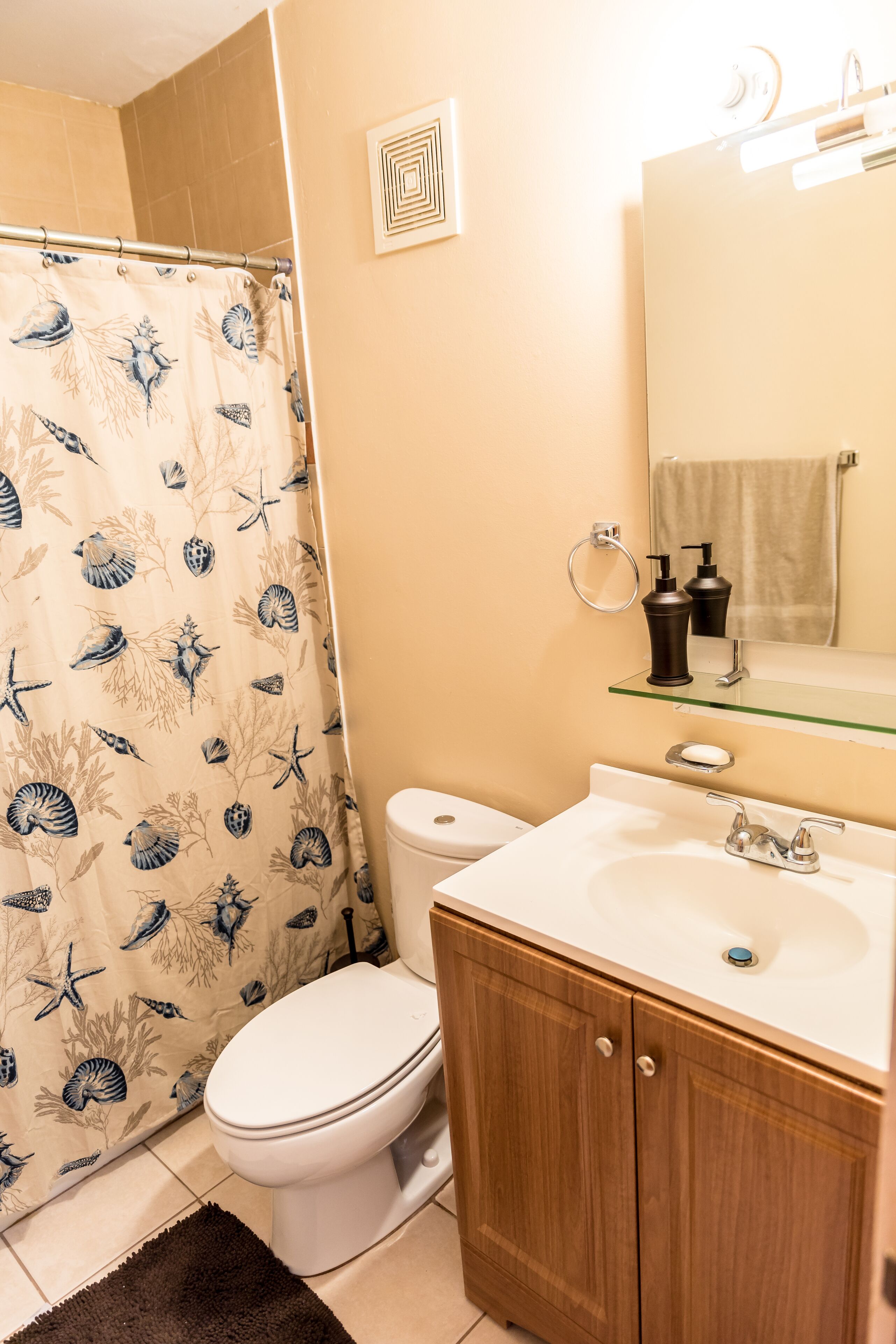 A bathroom with a toilet, a shower curtain with a sea life pattern, a sink with a mirror above it, and wooden cabinets.