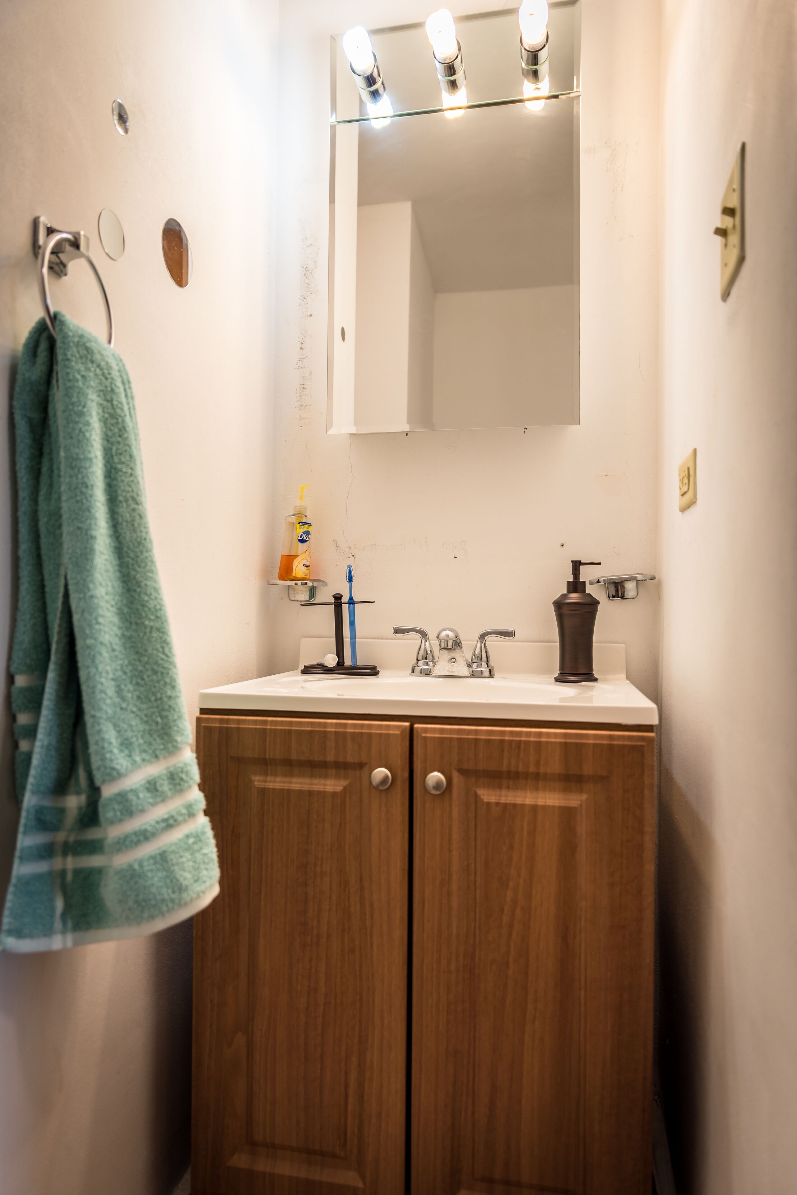 Un baño con tocador de madera, espejo, toallero, porta cepillos de dientes y dispensador de jabón.