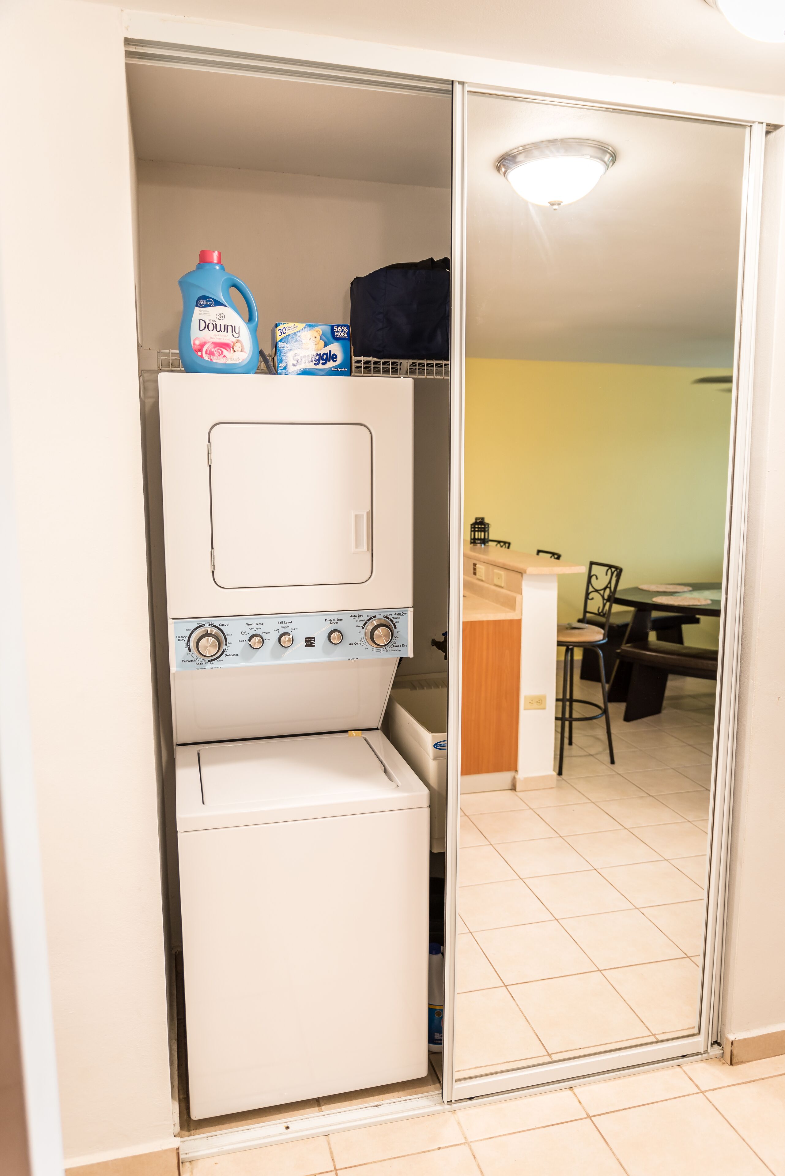 A compact laundry room with a washing machine and a dryer, a small kitchenette with a sink and a stove, and a dining area with a table and chairs.