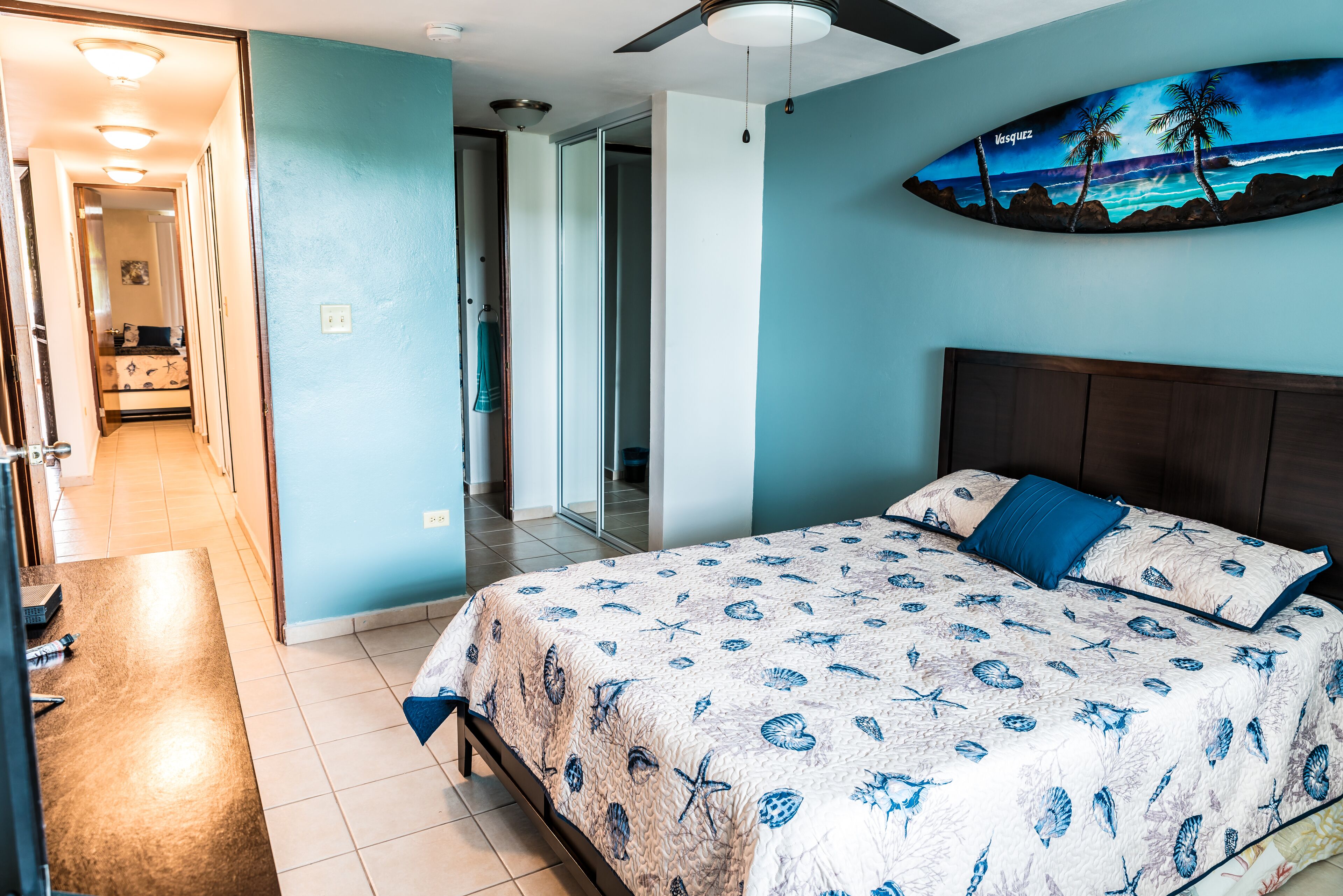 Une chambre avec un lit, un ventilateur de plafond et une décoration murale représentant une planche de surf.