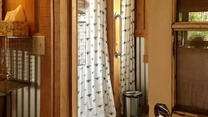 Un intérieur en bois comprenant un espace douche, une poubelle en métal et une porte munie d’une moustiquaire.