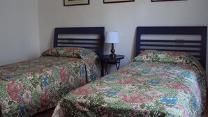 A room with two single beds, each with floral bedding, a small bedside table with a lamp, and three framed pictures on the wall. - The Palms Apartment (Piombino (LI))